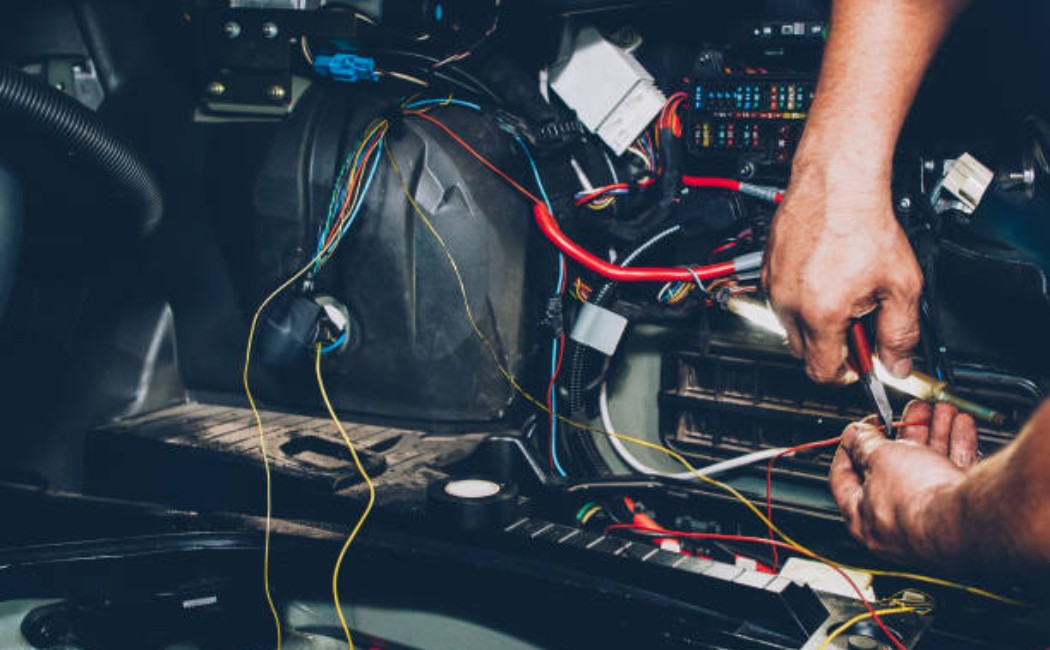 Auto service electrician wiring the underside of a car during maintenance.