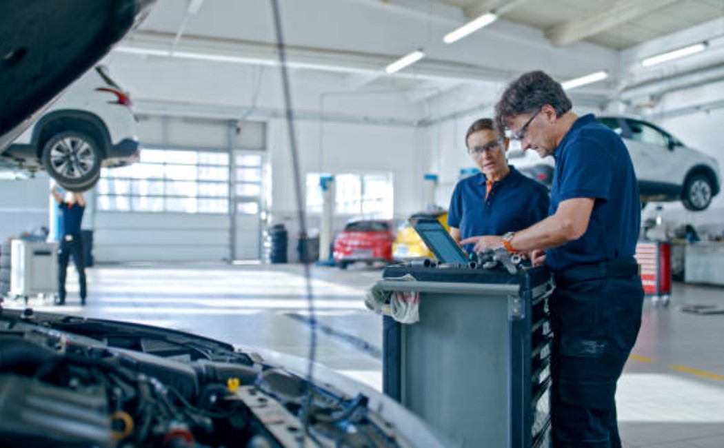 A mechanic and a manager reviewing engine diagnostics on a laptop in an auto workshop.