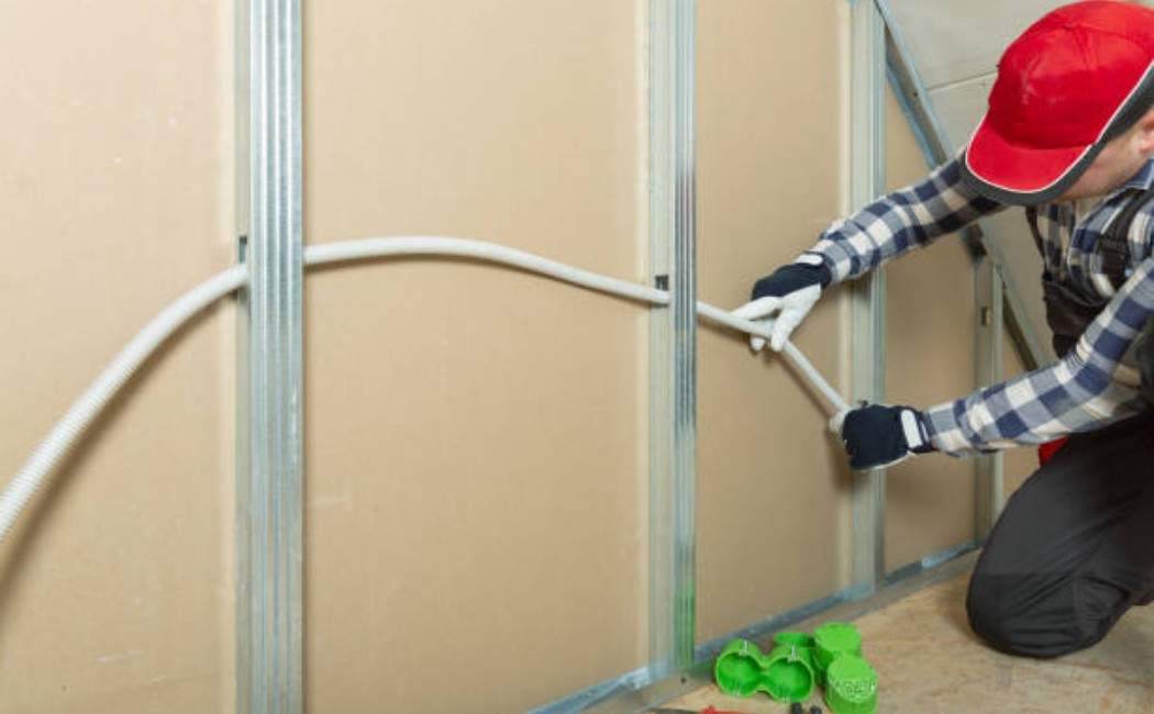 Professional electrician at work wiring attic walls in residential home.