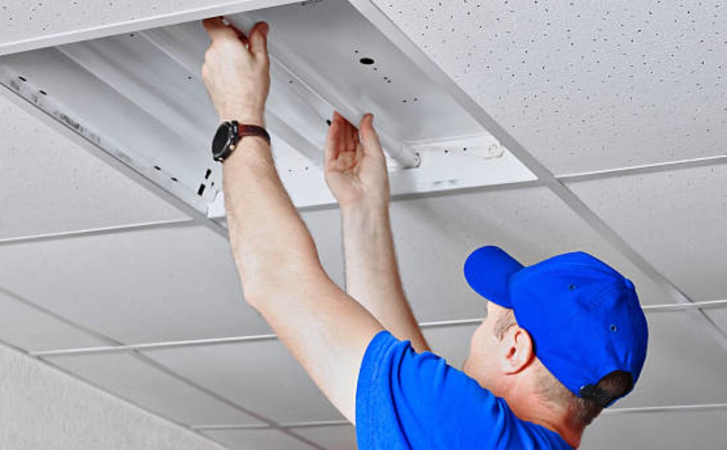 Maintenance worker installing a light fixture in the office interior